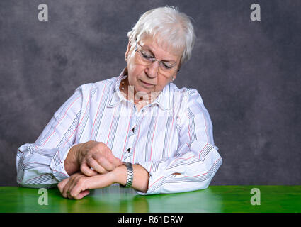 Grau behaarte ältere Frau stellen sie Ihre Uhr Stockfoto