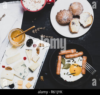 Gebratenes Huhn Eier und Würstchen in ein schwarzes Geschirr gusseisernen Pfanne auf einem schwarzen Holz Tisch, leeren Raum, Frühstück für 1 Stockfoto