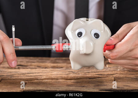 Unternehmer quetschen Sparschwein in Werkzeug spannen am Schreibtisch Stockfoto