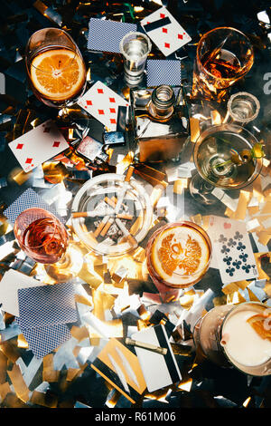 Blick von oben auf die Zigaretten, alkoholische Cocktails, Karten spielen, gerollte Banknoten, Kreditkarten und Kokain auf Tabelle von golden Konfetti bedeckt Stockfoto