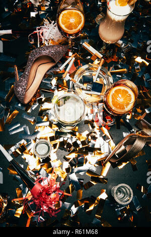 Ansicht der weiblichen Schuhe auf High Heel, Aschenbecher mit Zigaretten, alkoholische Cocktails und Party Hörner auf Tabelle von golden Konfetti bedeckt Stockfoto