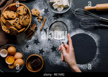 Teilweise mit Blick auf die Frau sieben Mehl durch Sieb über Tabelle von Mehl mit Symbolen der Sterne und Cookies mit Zutaten abgedeckt Stockfoto