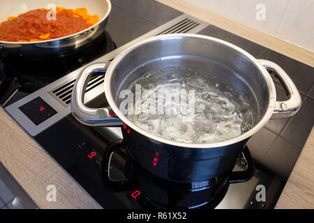 Topf mit kochendem Wasser und Pfanne bei Herd Stockfoto