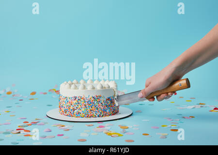 7/8-Ansicht von Frau schneiden leckeren Kuchen auf blauem Hintergrund Stockfoto