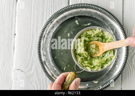 Geriebene Gurken im Sieb mit hölzernen Löffel Draufsicht Stockfoto