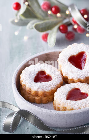 Close-up auf traditionelle weihnachtliche Linzer Plätzchen mit Erdbeermarmelade in Beton Platte am weißen Tisch gefüllt mit Weihnachten Dekorationen Stockfoto