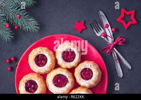 Mini bundt ring Kuchen mit roten whortleberry Stau auf dunklem Hintergrund mit Tannen Zweigen und Beeren. Weihnachten süße Speisen. Stockfoto