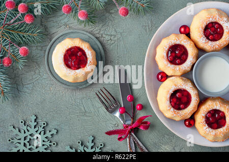 Mini bundt ring Kuchen mit roten whortleberry Stau auf Grün strukturierten Hintergrund mit fir Zweige, Beeren und Schneeflocken. Weihnachten süße Speisen. Stockfoto