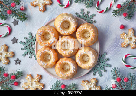 Mini bundt ring Kuchen mit Puderzucker auf hellen Hintergrund mit fir Zweige, Beeren und Zuckerstangen. Weihnachten süße Speisen. Stockfoto