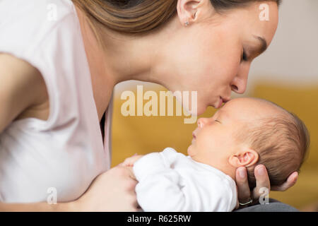 Liebevolle Mutter Kuscheln Baby Sohn und ihm auf die Stirn Küssen Stockfoto