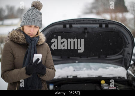 Weibliche Autofahrer Aufgeschlüsselt im Schnee für Pannenhilfe auf Handy Stockfoto