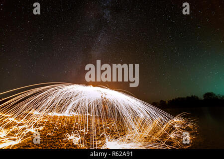 Licht malerei Kunst Konzept. Die Spinnerei Stahlwolle in abstrakten Kreis, Feuerwerk Duschen von hellen gelb leuchtenden funkelt in Brunnen Form am Flussufer Stockfoto