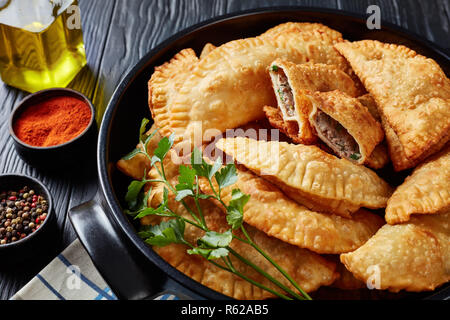 In der Nähe von Deep fried Umsätze oder Chebureki mit einer Füllung aus Hackfleisch und Zwiebel in eine schwarze Keramik Topf auf einem Holztisch, horizontale Ansicht aus einem Stockfoto