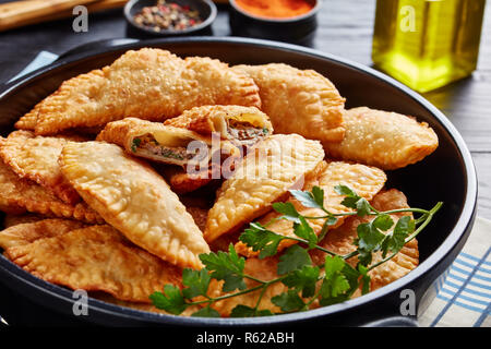 Frittierte Umsätze oder Chebureki mit einer Füllung aus Hackfleisch und Zwiebel in eine schwarze Keramik Topf auf einem Holztisch, horizontale Ansicht von oben, Schließen - Stockfoto