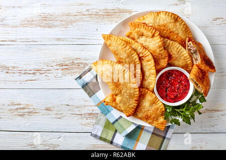 Leckere frittierte Umsätze oder Chebureki mit Hackfleisch, Zwiebeln und Kräuter Füllung auf eine weisse Platte auf einem Holztisch, horizontale Ansicht von oben, c Stockfoto