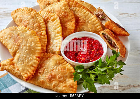 Leckere frittierte Umsätze oder Chebureki mit Hackfleisch, Zwiebeln und Kräuter Füllung auf eine weisse Platte auf einem Holztisch, horizontale Ansicht von oben, c Stockfoto