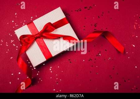 Handwerk Geschenkbox mit roter Schleife auf fesrive Roter Hintergrund mit funkelt. Stockfoto