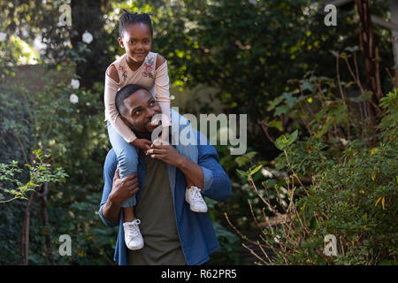 Ein Mädchen sitzen auf den Schultern ihrer Väter in einem Garten Stockfoto
