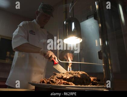 Brig. Gen. Robert G. Novotny, 57 Wing Commander, Schnitte Essen für die Gäste des Seitenwind Inn Speisesaal an der Nellis Air Force Base, Nev, Nov. 22, 2018. Kommandanten, Nellis Personal und ihre Familien serviert Thanksgiving Dinner für Flieger, die von ihren Familien im Urlaub. Stockfoto