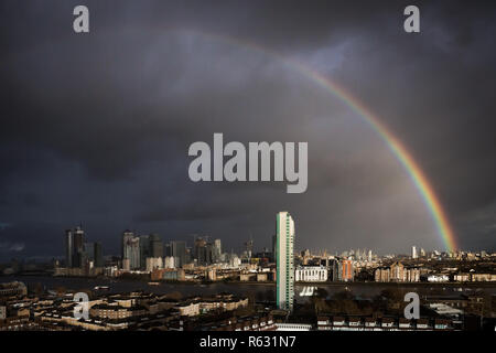 London, Großbritannien. 3. Dezember, 2018. UK Wetter: Eine massive Regenbogen bricht über East London einschließlich Canary Wharf business park Gebäude während eines kurzen Nachmittag Regensturm. Credit: Guy Corbishley/Alamy leben Nachrichten Stockfoto