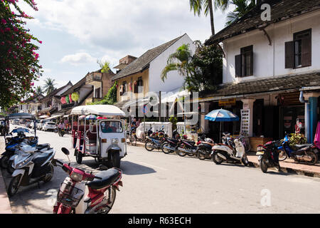 Street Scene mit dem Tuk Tuk und Roller außerhalb der Geschäfte im kolonialen Stadtteil der alten Stadt. Sisavangvong Straße, Luang Prabang, Louangphabang Provinz, Laos Stockfoto
