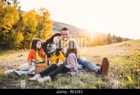 Eine junge Familie mit zwei kleinen Kindern in Picknick im Herbst Natur bei Sonnenuntergang. Stockfoto