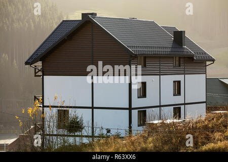 Neue schöne weiße und braune zweistöckiges Ferienhaus mit Schindeldach im ökologischen Bereich auf nebligen Wald und Hügel Hintergrund auf sonnigen Sommertag. Auch maintai Stockfoto