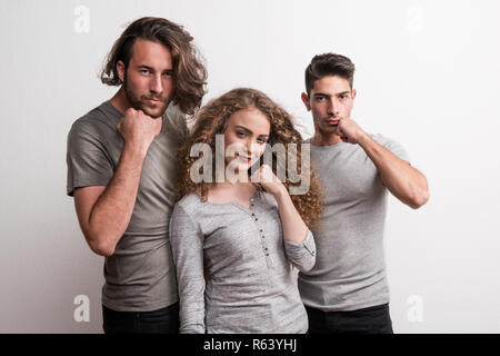 Portrait von fröhlichen jungen Mädchen mit zwei junge Freunde stehen in einem Studio, Faust gegen Gesicht. Stockfoto