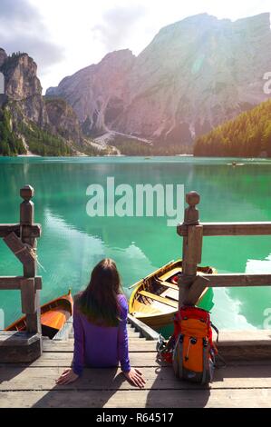 Mädchen Backpacker sitzen auf einem Pier und Pragser See, Dolomiten Italien Stockfoto