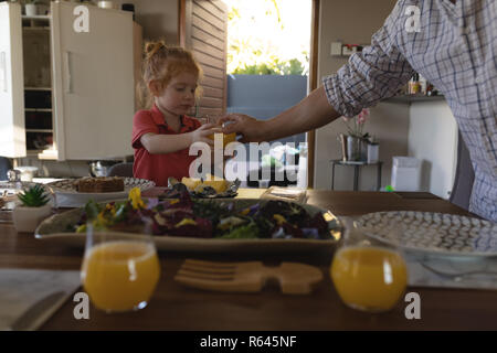 Vater mit Orangensaft zu seiner Tochter auf Esstisch Stockfoto