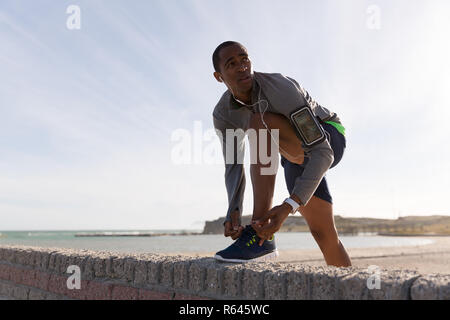 Männliche Athlet seine Schnürsenkel binden auf umgebende Mauer Stockfoto