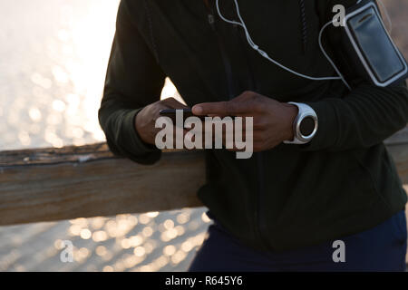 Männliche Athlet mit Handy auf Pier Stockfoto