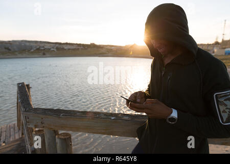 Männliche Athlet mit Handy auf Pier Stockfoto