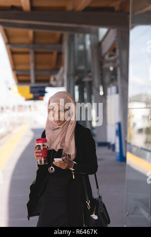 Frau mit Handy während Kaffee in der Plattform am Bahnhof Stockfoto