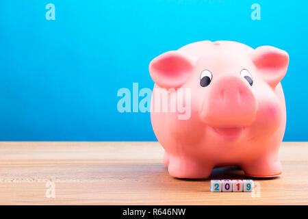 2019 finanzielle Ziel, glücklich lächelnde rosa Sparschwein mit Holz cube Block mit der Nummer 2019 auf hölzernen Tisch Stockfoto