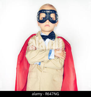 Adorable kleinen Jungen Superhelden in Anzug und Fliege trägt einen roten Mantel und Brille suchen mutige während vor einem weißen Hintergrund stehen Stockfoto