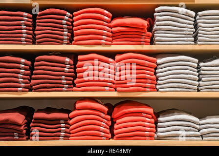 Kleidung angezeigt. Kopieren spase für Text. Viele warme Pullover von heller Farbe sind ordentlich in einer Reihe auf den Regalen gestapelt. Stapel der Bunte gestrickte wollene Kleidung. T-Shirt auf die lange Bank schieben Stockfoto