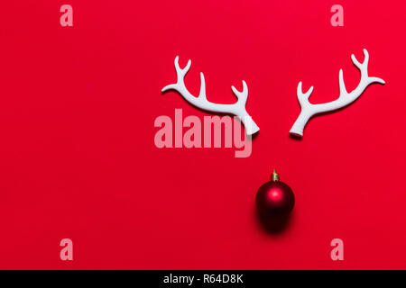 Festliche rentier Gesicht aus weissem Geweih und eine Weihnachtskugel auf rotem Hintergrund Stockfoto