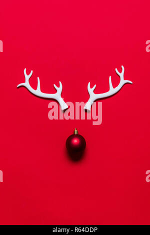 Festliche rentier Gesicht aus weissem Geweih und eine Weihnachtskugel auf rotem Hintergrund Stockfoto