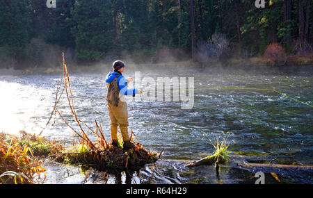 Ein Morgen, Nebel steigt aus dem Metolius River in den Cascade Mountains von Oregon, während ein Fliegenfischer wirft für die Regenbogenforelle im kalten Wasser. Stockfoto