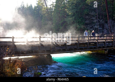 Ein Morgen, Nebel steigt aus dem Metolius River in den Cascade Mountains von Oregon, während zwei Wanderer die Aussicht genießen. Stockfoto