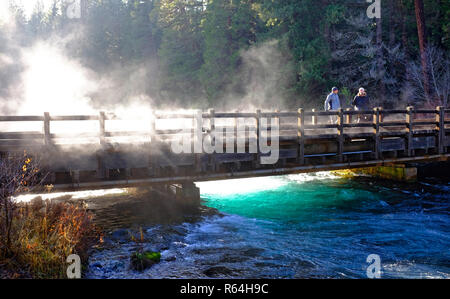 Ein Morgen, Nebel steigt aus dem Metolius River in den Cascade Mountains von Oregon, während zwei Wanderer die Aussicht genießen. Stockfoto