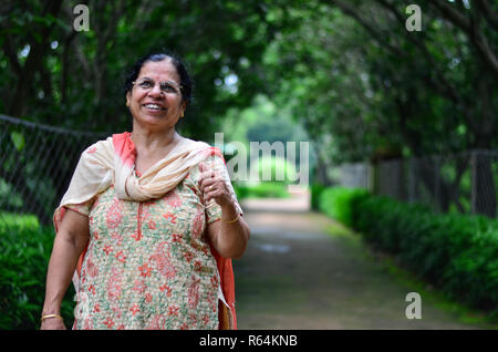 Portraitfotos von einer glücklichen suchen Senior nördlich der indischen Frau, die traditionelle indische Salwar Kamiz nach oben in einem Garten. Stockfoto