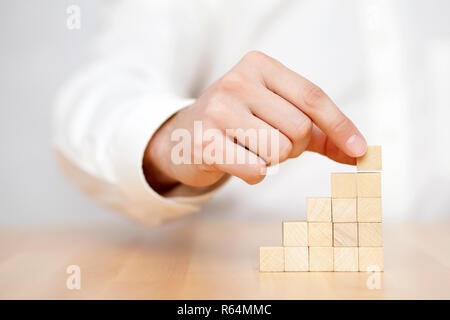 Die Hand des Menschen legen Sie Holzblöcke in der Form einer Treppe. Geschäftlicher Erfolg Konzept. Stockfoto