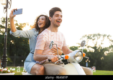 Porträt der lächelnde Frau, die auf dem Smartphone selfie beim Reiten auf dem Motorrad durch die Stadt Straße zusammen mit ihrem Freund Stockfoto