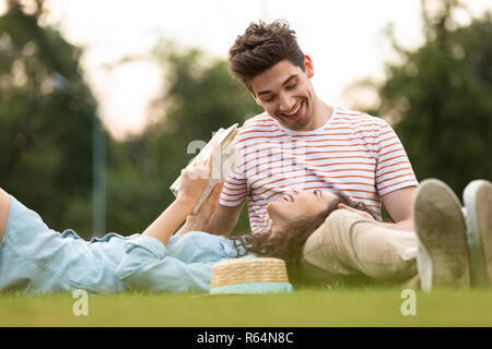 Bild der glücklichen Paar Mann und Frau 20s auf grünem Gras im Park und lesen Buch Stockfoto