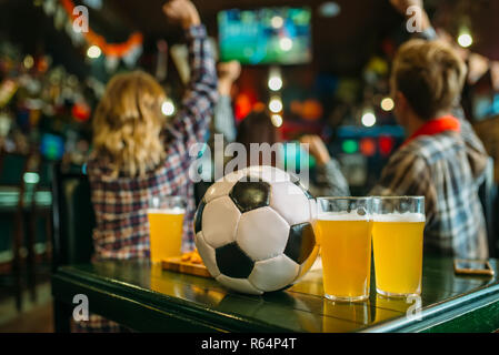 Kugel und Bier auf dem Tisch in der Sports Bar, Fußball Fans im Hintergrund. Die TV-Ausstrahlung, die das Spiel beobachten, Konzept Stockfoto