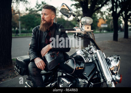 Baerded biker stellt auf der Häckslerwelle, lehnte sich auf einen Helm. Vintage bike, Fahrer und seinem Motorrad, Freiheit Lifestyle, Radtouren Stockfoto