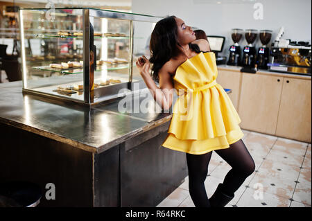 Stilvolle afrikanische amerikanische Frau an gelben dreess stellte im Coffee House. Stockfoto