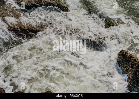 Yarada Strand mit indischen Ozeanwellen, die auf die Uferfelsen und -Steine krachen. Langzeitbelichtung mit seidig glattem Wasser und Felsen im Hintergrund. Stockfoto